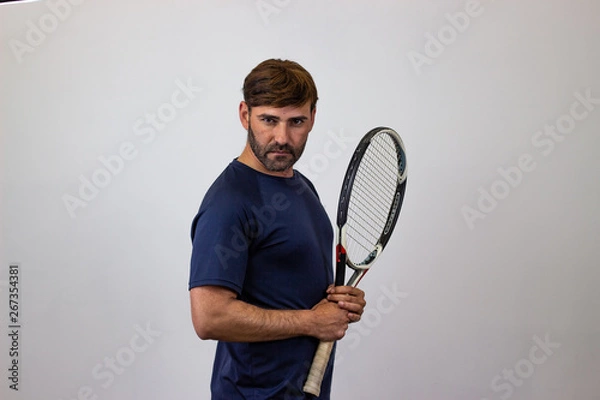 Fototapeta Portrait of handsome young man playing tennis holding a racket with brown hair showing bad face, their back facing the camera and looking at the camera. Isolated on white background.