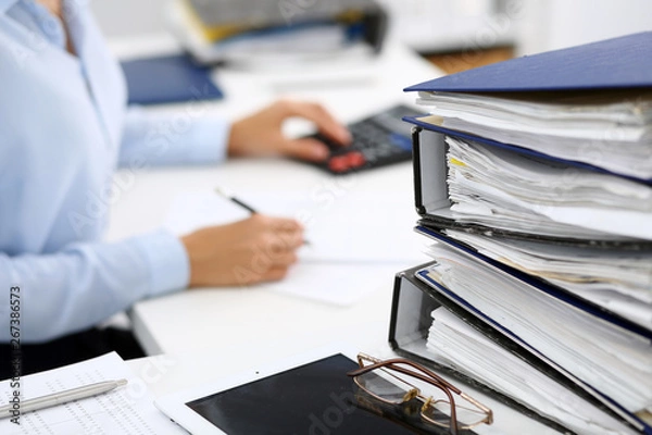 Fototapeta Binders with papers are waiting to be processed by business woman or bookkeeper back in blur. Internal Audit and tax concept