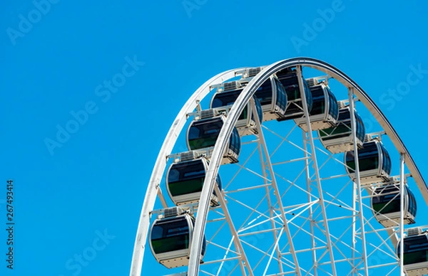Fototapeta Closeup modern Ferris wheel against blue sky and white clouds. Ferris wheel at funfair for entertainment and recreation on holiday. Modern construction of Ferris wheel in amusement. Fun festival.