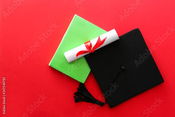 Fototapeta Mortar board, diploma and book on color background. Concept of high school graduation