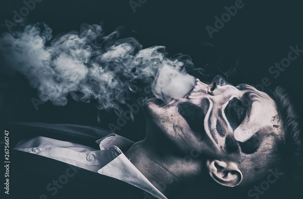 Fototapeta Stylish and beautiful, emotional young man with skeleton makeup in a strict suit against the background of smoke and dark background to Halloween
