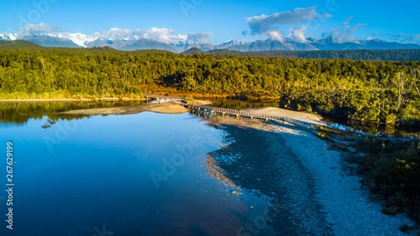 Fototapeta Small bridge across a river surrounded by native forest at the coastline of Tasman sea. West Coast, South Island, New Zealand