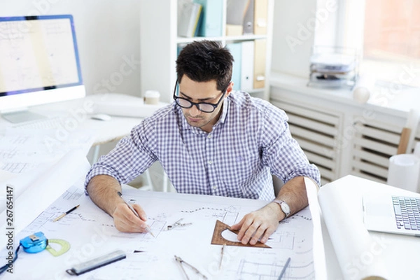 Fototapeta Portrait of young engineer drawing plans and making measurements at workplace, copy space