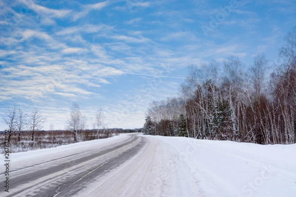 Fototapeta Patterns on the winter highway in the form of four straight lines. Snowy road on the background of snow-covered forest. Winter landscape.