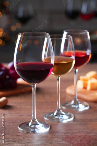 Fototapeta Glasses with different wines and appetizers on wooden table against blurred background