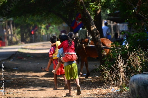 Obraz カンボジアのクラチェ　メコン川沿いの村　大きな子供が小さな子供をおんぶする姿　路上に佇む馬