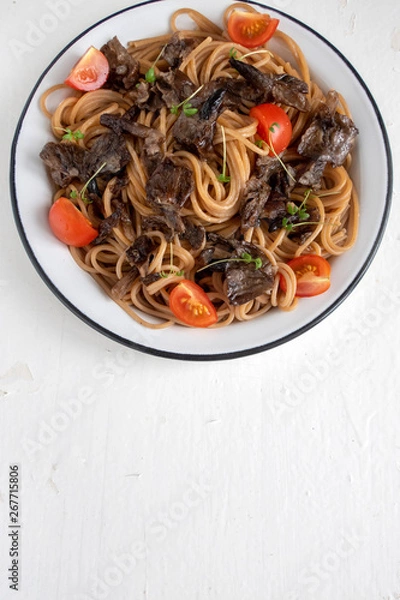 Obraz Brown buckwheat spaghetti with mushrooms, tomato and watercress salad on a light wooden background, healthy food concept. Close-up and copy space. Top view. Vertical