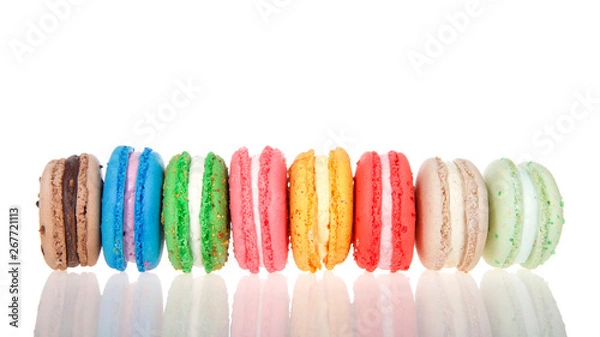 Fototapeta Row of macaron cookies laying sideways side by side multiple colors and flavors on a reflective surface isolated on white. Traditional french treat.