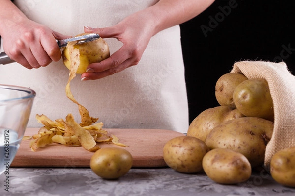 Obraz A young woman in an apron peeling potatoes
