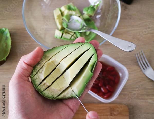 Obraz Holding an avocado half in the hand, slicing avocado for a dip