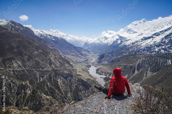 Fototapeta Explorer concept: Man wearing red jacket seating on the edge of a clift in Thorong-La Base Camp located in Annapurna Circuit