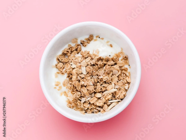 Fototapeta Whole grains on yogurt in white bowl, pink background.