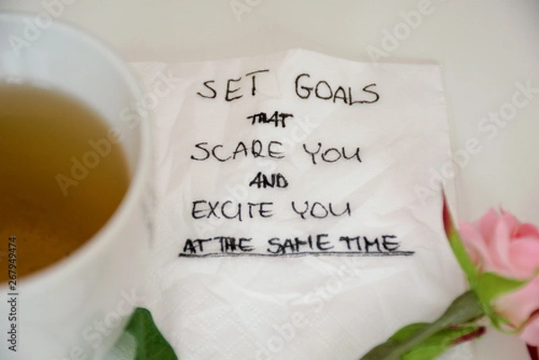 Obraz Planning motivational quote on white napkin on white table with tea, rose and pen. Set goals that scare you and excite you at the same time