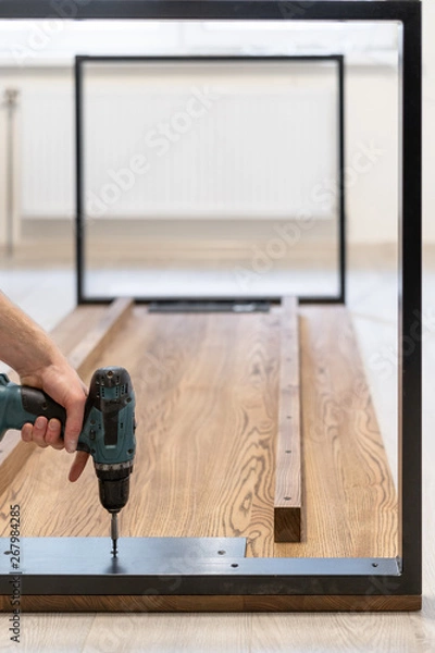 Fototapeta Man using screwdriver fasten metal element on wooden table top