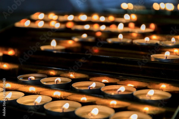Fototapeta Many burning candles with shallow depth of field. Candles light background. Candle flame at night.