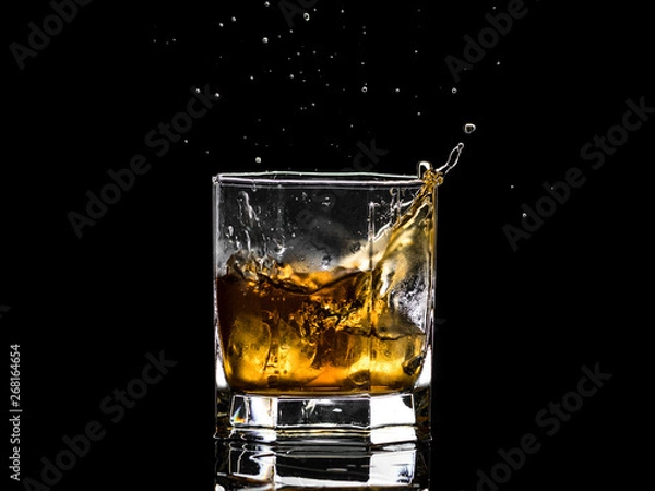 Fototapeta Hexagonal glass of whiskey brandy with ice and splashes from falling ice