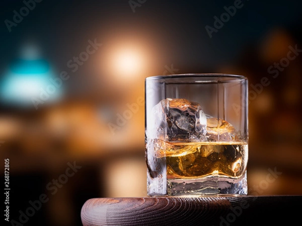 Fototapeta Glass of whiskey with ice cubes on the wooden table with city view background