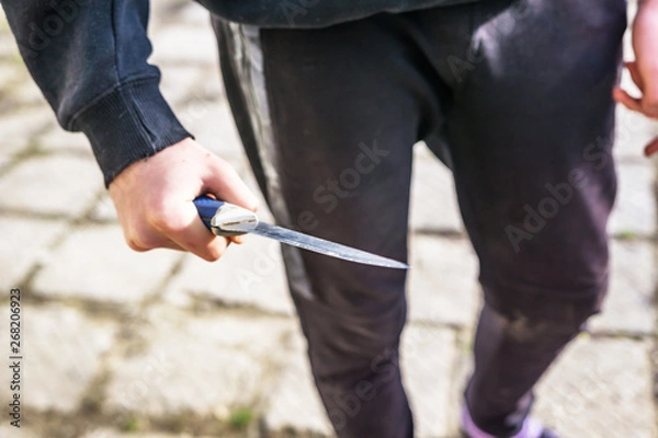 Fototapeta Close-up of a young man's hand with a knife, a big blade. Arrogance and violence among young people. Shallow depth of focus.