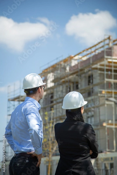 Fototapeta Two architects a man and a woman in construction in white helmets.