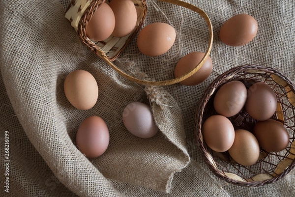 Obraz eggs placed  in a egg carton and  а wicker basket over a tat