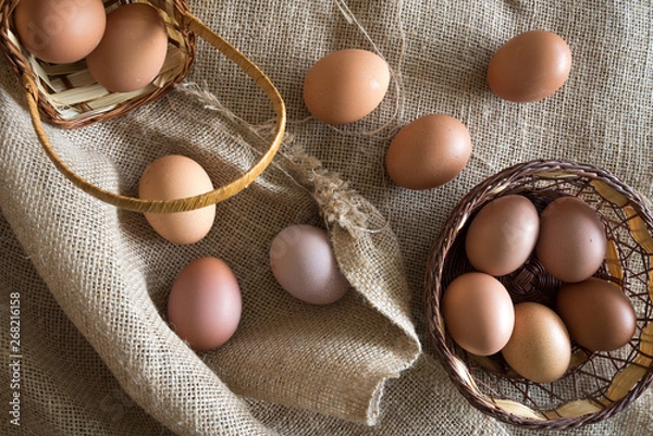 Obraz eggs placed  in a egg carton and  а wicker basket over a tat
