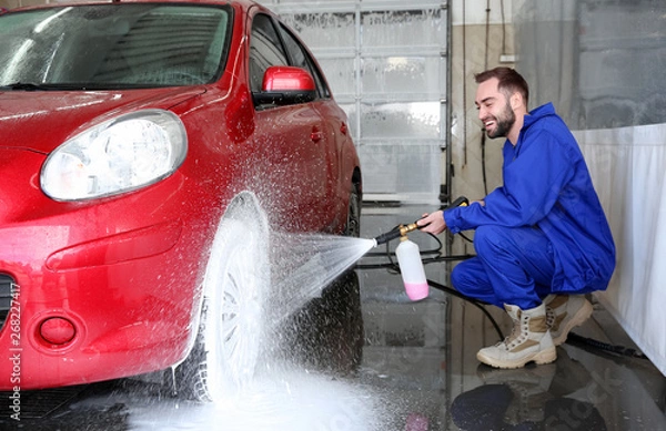 Fototapeta Worker cleaning automobile with high pressure water jet at car wash