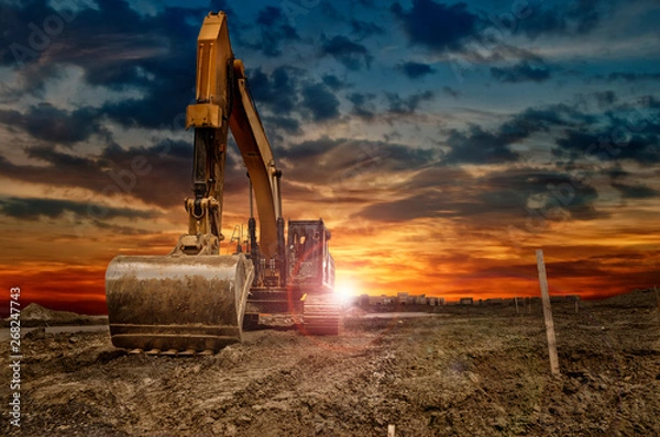 Obraz Excavating machinery at the construction site, sunset in background.