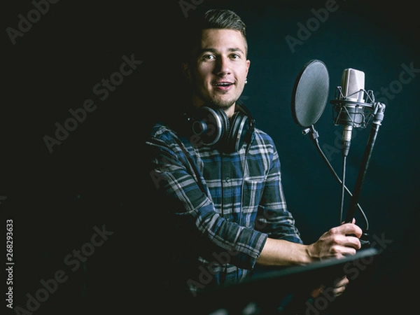 Fototapeta The young guy singing in recording studio
