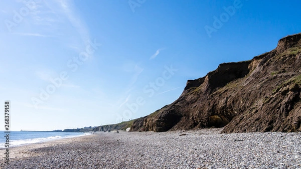 Obraz Panorama of cliff faces made of rock and earth at Seaham Hall Beach in County Durham showing blue sky, pebbled beach and a calm North Sea.