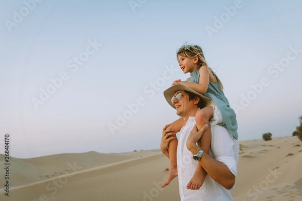 Obraz Little girl sitting on dad's shoulders and looking at the sunset in the desert