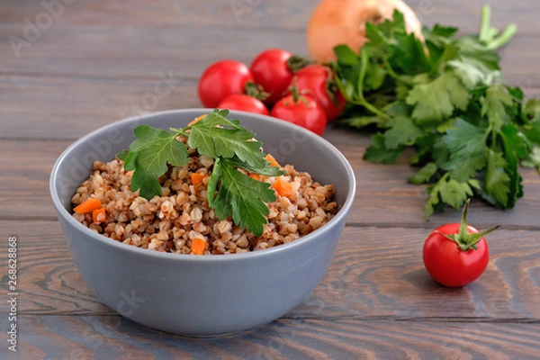 Obraz Buckwheat porridge with a sprig of parsley in a bowl and tomatoes on a dark rough wooden table. Rustic style. Traditional Russian dish.  Russian porridge