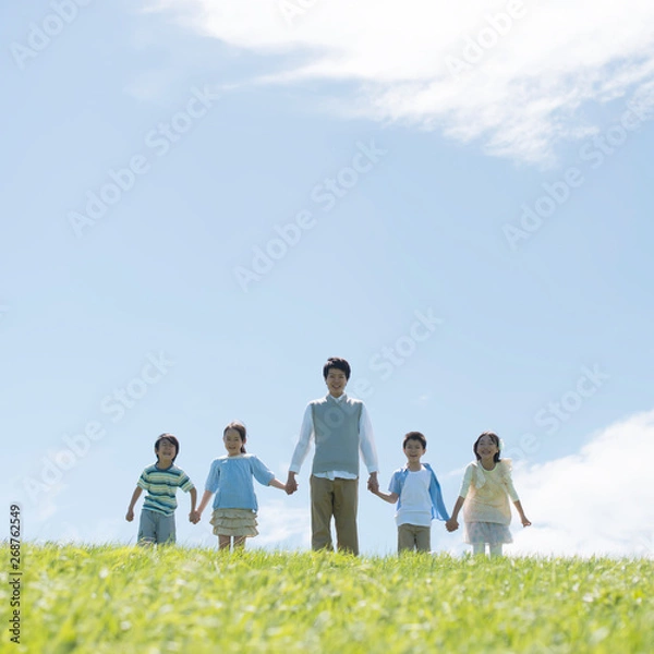 Fototapeta 草原で手をつなぐ小学生と先生