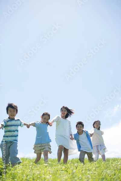 Fototapeta 草原で手をつなぐ小学生と先生