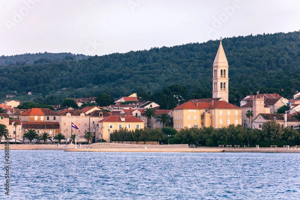 Fototapeta Supetar city in Brac island, Croatia. View from the sea. Picturesque scenic view on Supetar on Brac island, Croatia. Panoramic view on harbor of town Supetar from the side of sea. Brac, Croatia.