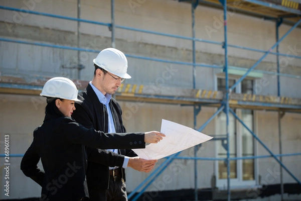 Fototapeta Two architects a man and a woman in construction in white helmets.