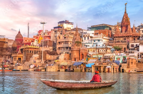 Obraz Ancient Varanasi city architecture at sunset with view of sadhu baba enjoying a boat ride on river Ganges.