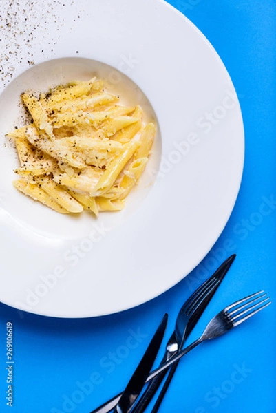 Obraz Pasta penne with cheese and creamy sauce on white plate on blue background. Italian cuisine.