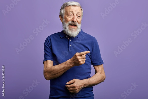 Fototapeta positive man pointing with hand and finger to the side. look here, happy old man showing direction, pension is being given here. this is the right way.