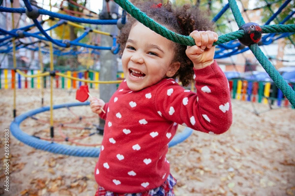 Fototapeta healthy african american little girl having a fun time. Crazy small kid bouncing back and forward in the playground outdoors