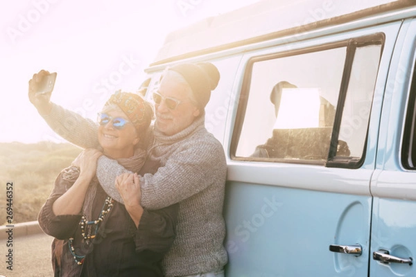 Obraz Travel and alternative people vacation concept for senior retired lifestyle couple taking selfie picture for social media - vintage van in background - sunset sunlight and forever concept