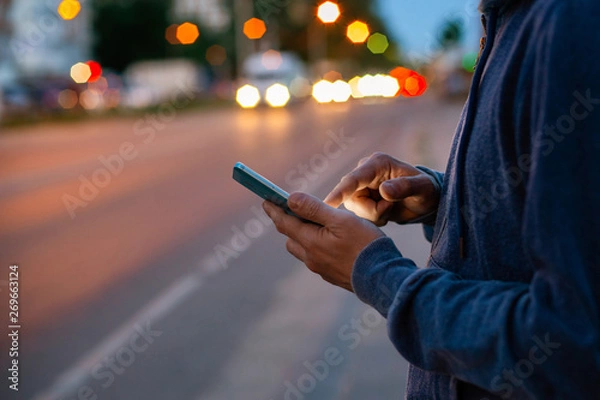 Fototapeta Hipster man talking on a mobile phone at night in the city against the background of bokeh lights.