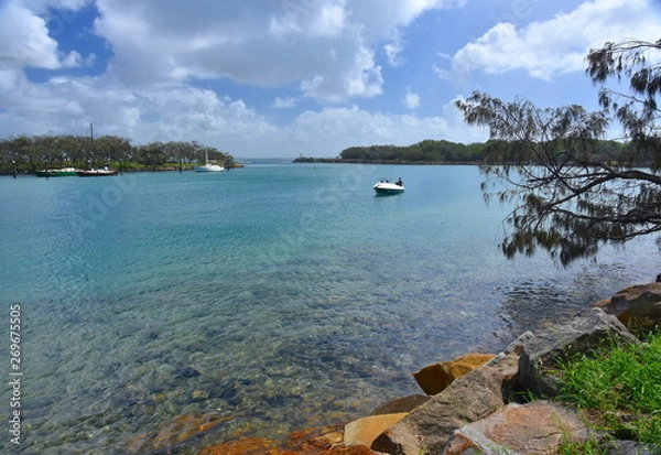 Obraz Boat on Mooloolah River on a sunny but cloudy day. Rock wall along Mooloolah river (Sunshine Coast, Queensland, Australia). Moored yachts in the marina.