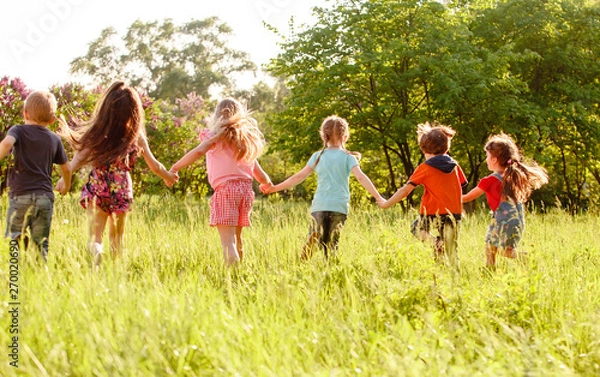 Fototapeta a group of children playing and running in the park on a green gozon.