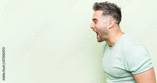 Fototapeta Young handsome man against a green background shouting towards a copy space