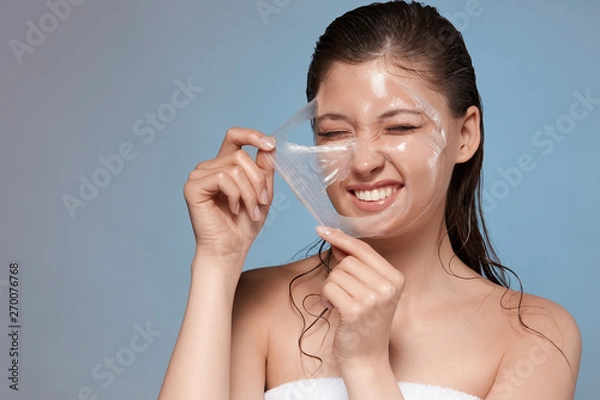 Fototapeta happy woman removing with hardness her facial mask and smiling, pretty young girl doing spa procedures, copy space