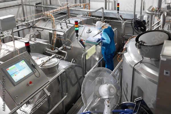 Obraz worker in a blue robe and a cap inspect the production department of dairy factory