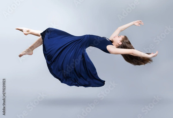 Obraz A girl in a blue dress is floating in the air. Dress and hair fluttering in the wind. Flight. Fantasy.