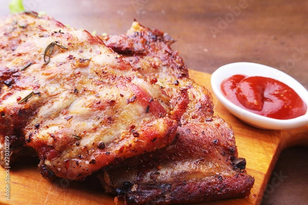 Obraz grilled barbecued ribs with lettuce leaves, hot chili pepper and sauce on wooden cutting board.