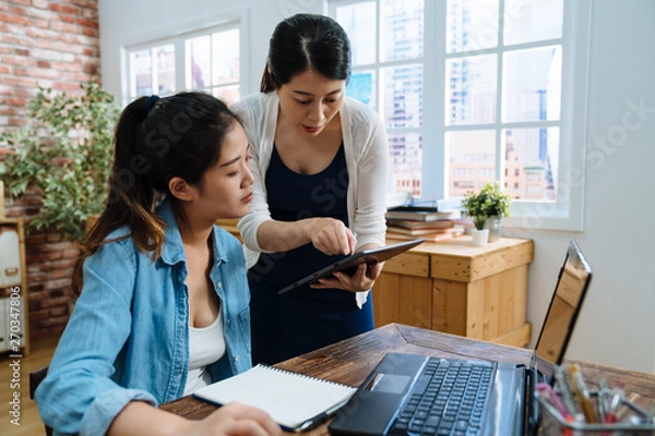 Fototapeta Young asian woman seller with coworker talking discussing point on mobile pad computer with customer for online business shopping shipping box package in modern bright office. pregnant lady worker