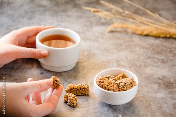 Fototapeta Gozinaki bars (Georgian Peanuts in sugar in white bowl and on gray background.The process of eating. In the hands of a young woman.Tea time concept